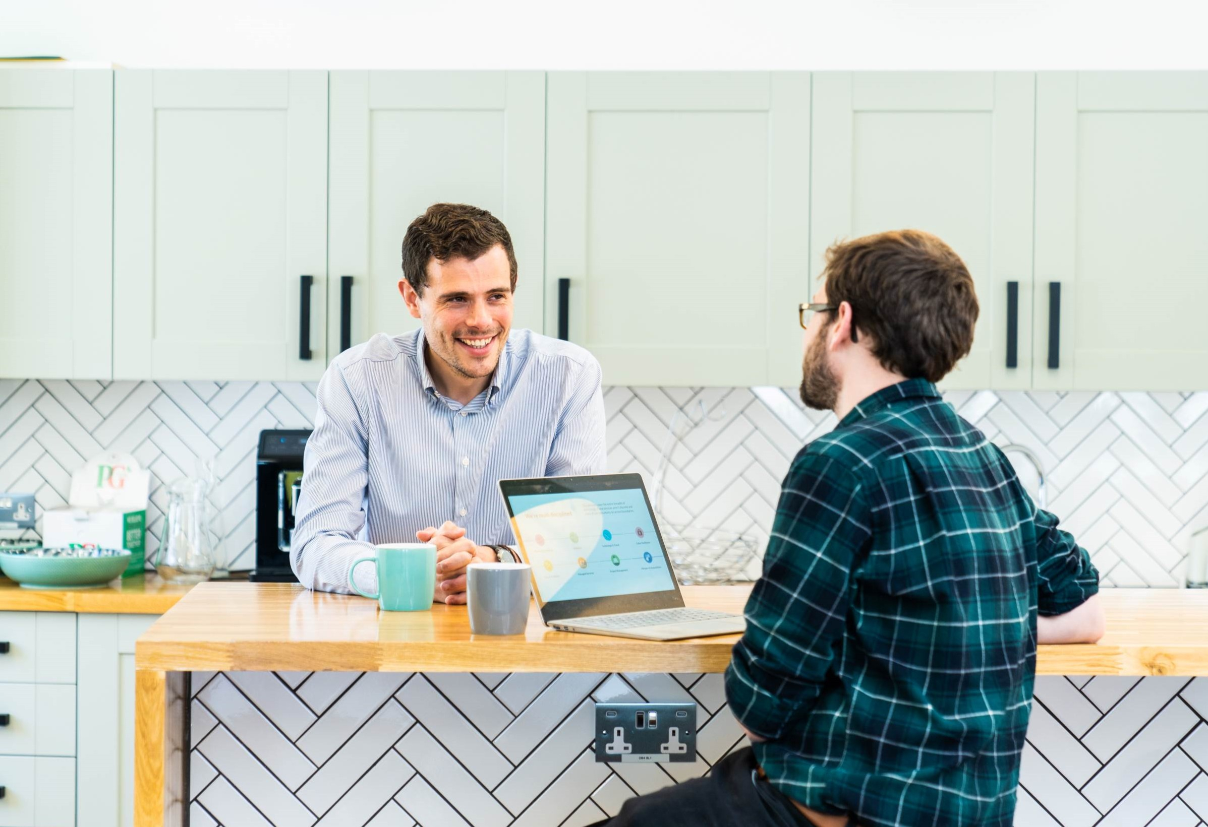 Two male colleagues chatting in a work kitchen space